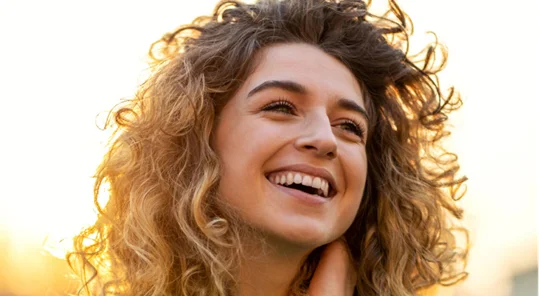 Smiling young woman with curly hair looking up and happy